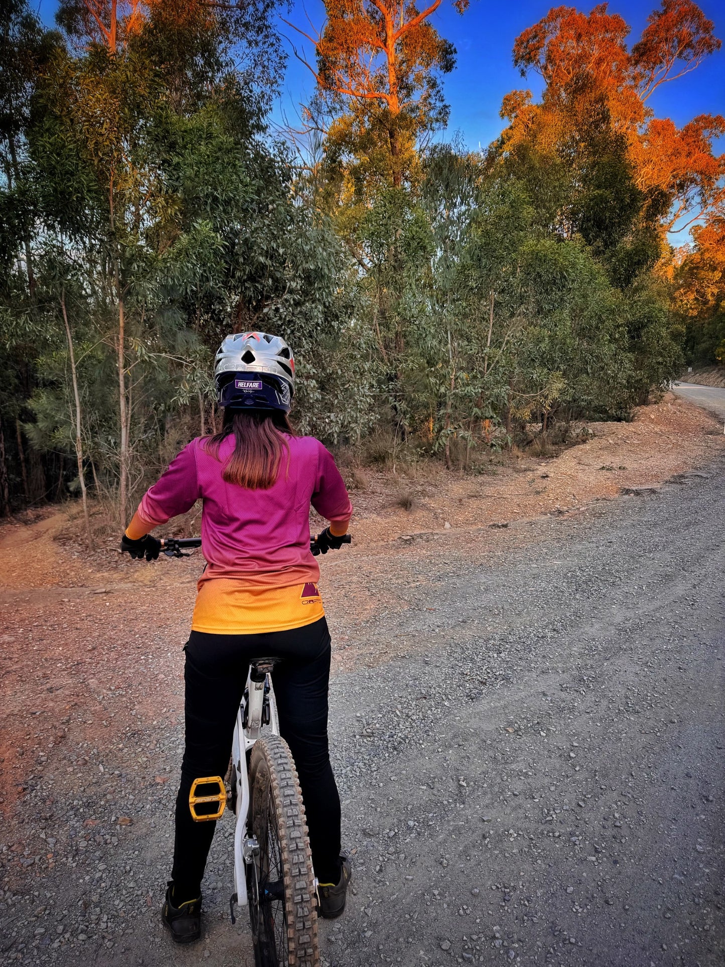 Person on a bike wearing a helmet on a forest path with autumn trees.