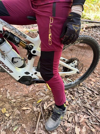 Close-up of CROFTO Women's Amaroo Lite maroon MTB pants with black knee panels, zipped pocket and gold CROFTO leg branding.