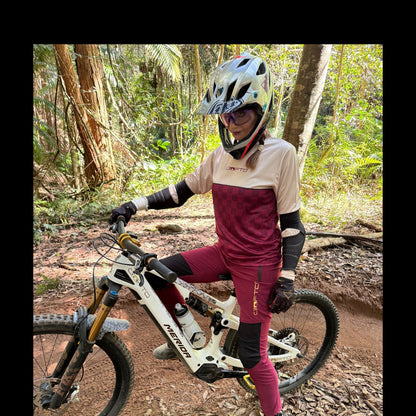 Rider wearing CROFTO Women's Amaroo Lite maroon MTB pants with black panels while seated on a mountain bike on a forest trail.