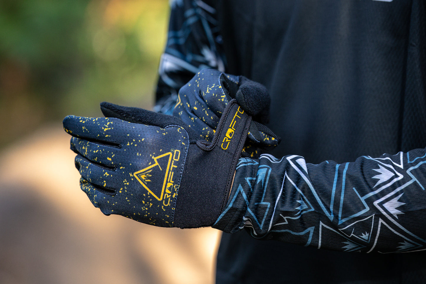 Close-up of a person wearing black and yellow CROFTO Apex Pro mountain biking gloves, with the brand logo and name clearly visible on the back of the glove.