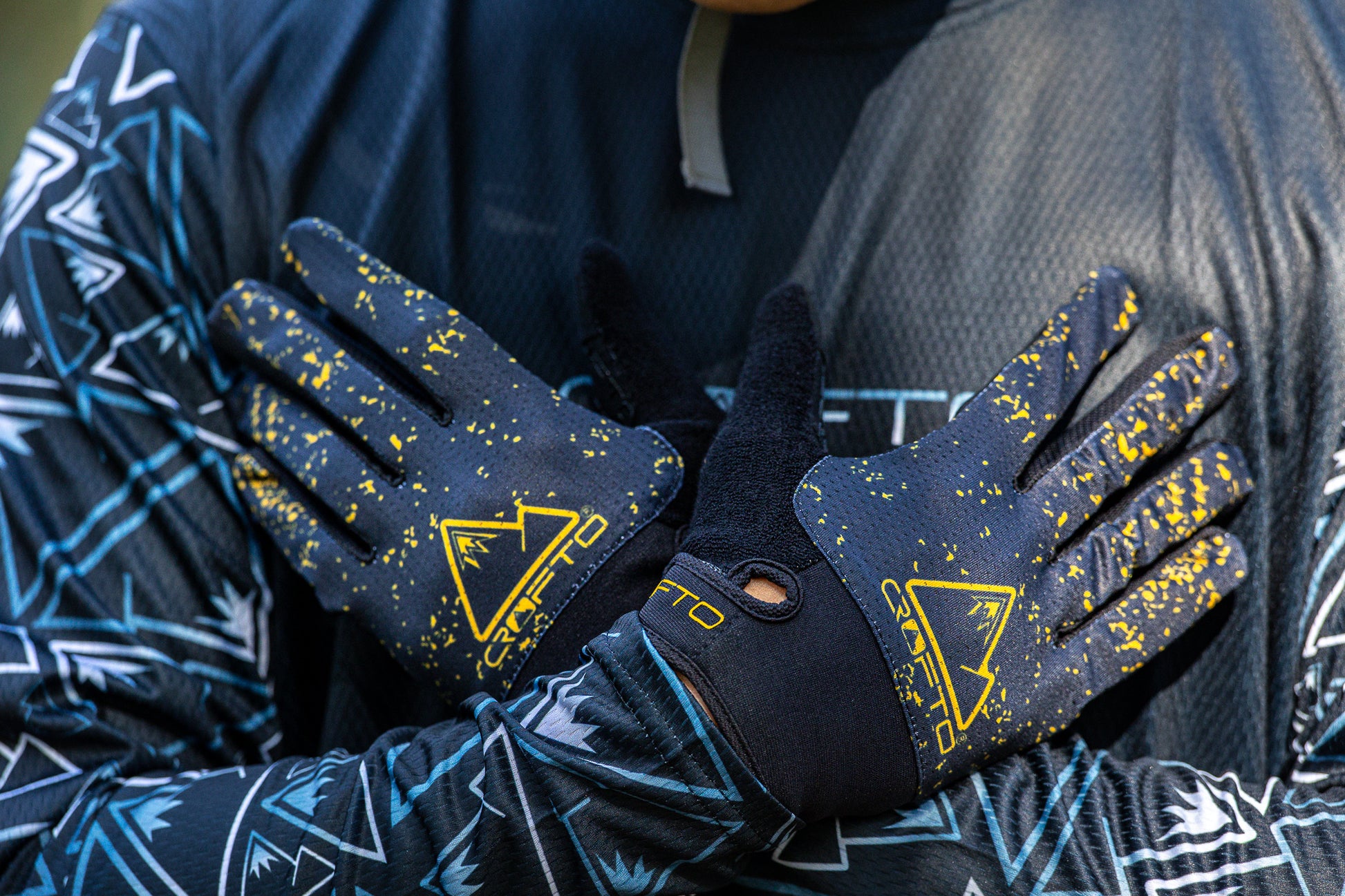 Close-up of a person wearing black and yellow CROFTO Apex Pro mountain biking gloves, held against his chest