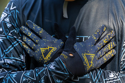 Close-up of a person wearing black and yellow CROFTO Apex Pro mountain biking gloves, held against his chest
