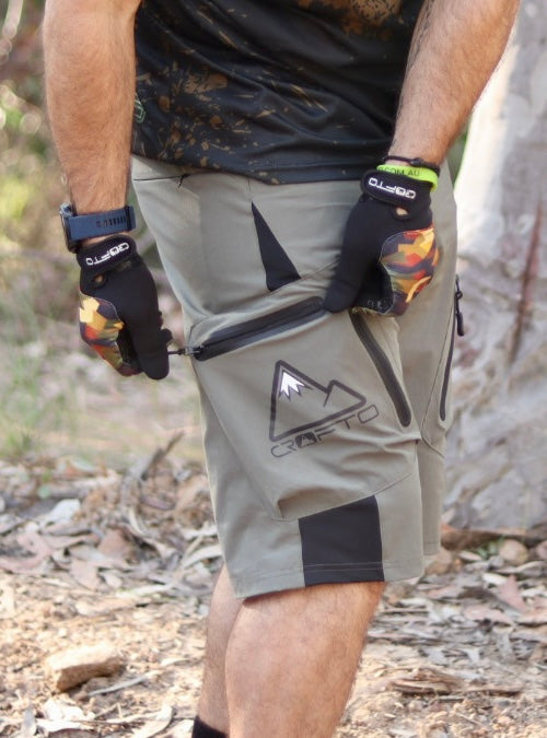 Close up of a person in a forest setting Opening the zip on a pocket of CROFTO Apex Pro Shorts 