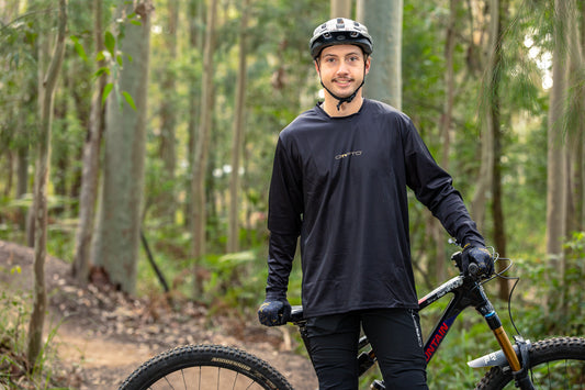 Rider wearing the CROFTO Enduro long sleeve mountain bike jersey in black while standing beside a mountain bike on a forest trail.