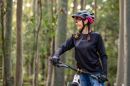 CROFTO Enduro black mountain bike jersey for trail, enduro and all-mountain riding, photographed beside a mountain bike in a forest setting.