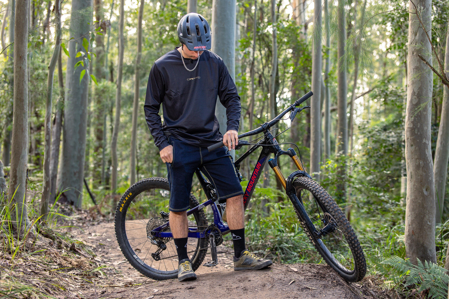 A person wearing a CROFTO Enduro MTB Jersey and CROFTO Denim MTB Jorts, standing next to a mountain bike in the Australia forest