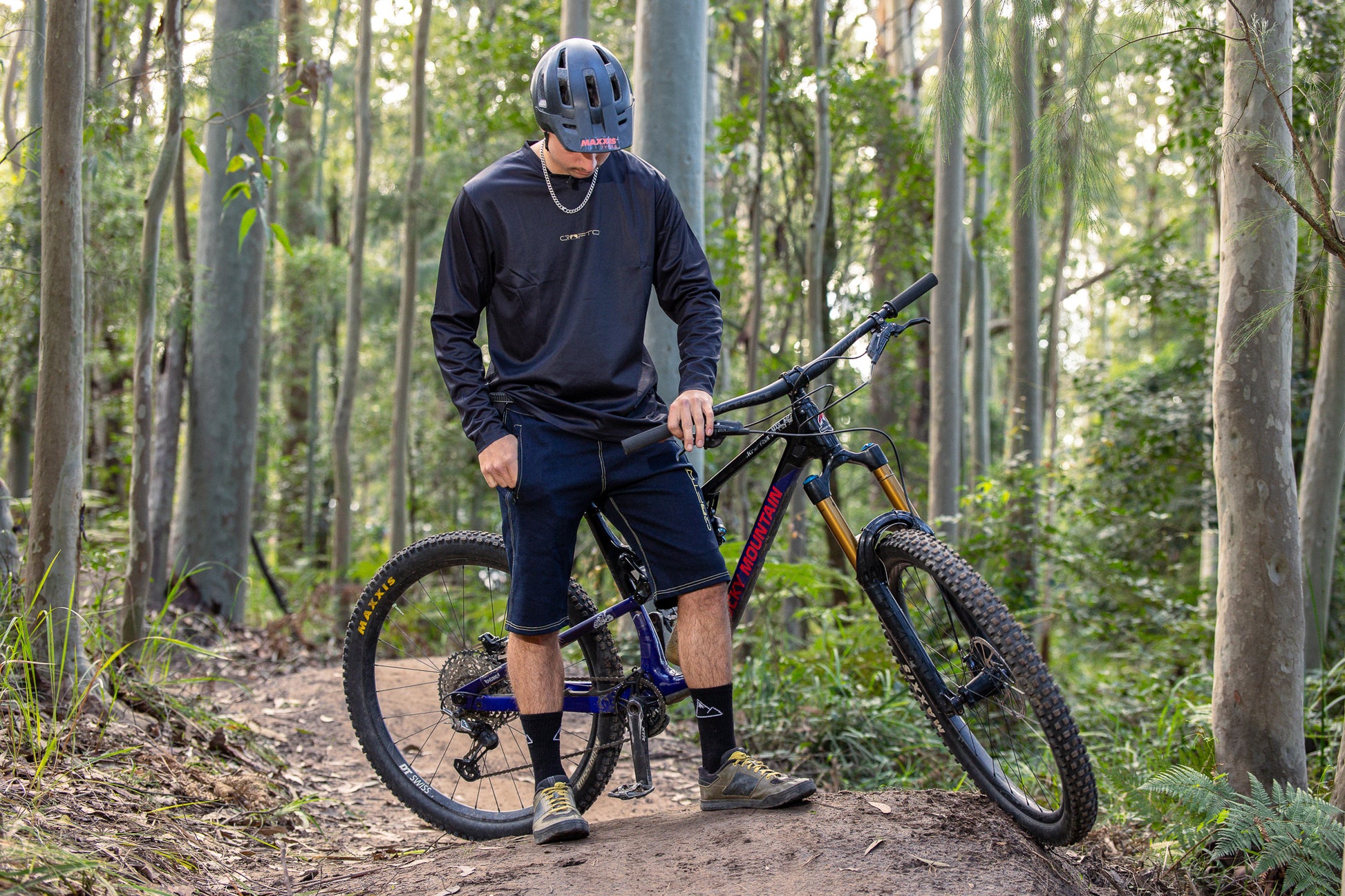 A person wearing a CROFTO Enduro MTB Jersey and CROFTO Denim MTB Jorts, standing next to a mountain bike in the Australia forest