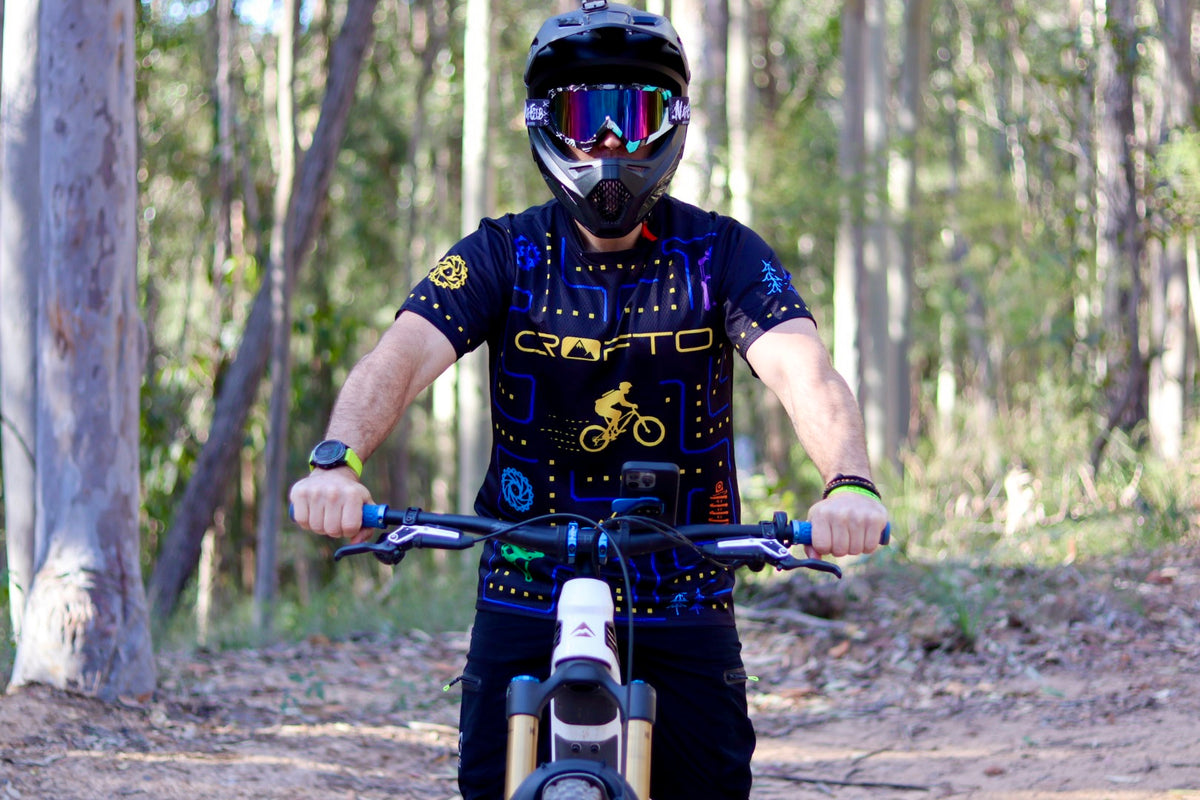 Rider wearing the CROFTO Trail Maze MTB jersey while sitting on a mountain bike on a forest trail.