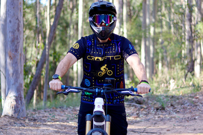 Rider wearing the CROFTO Trail Maze MTB jersey while sitting on a mountain bike on a forest trail.