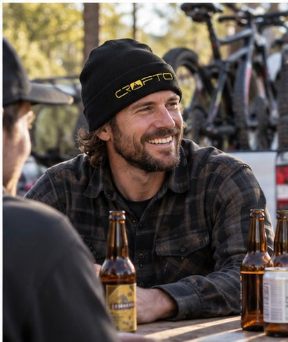 Mountain biker wearing a black CROFTO beanie while catching up with friends after a ride at the trailhead.