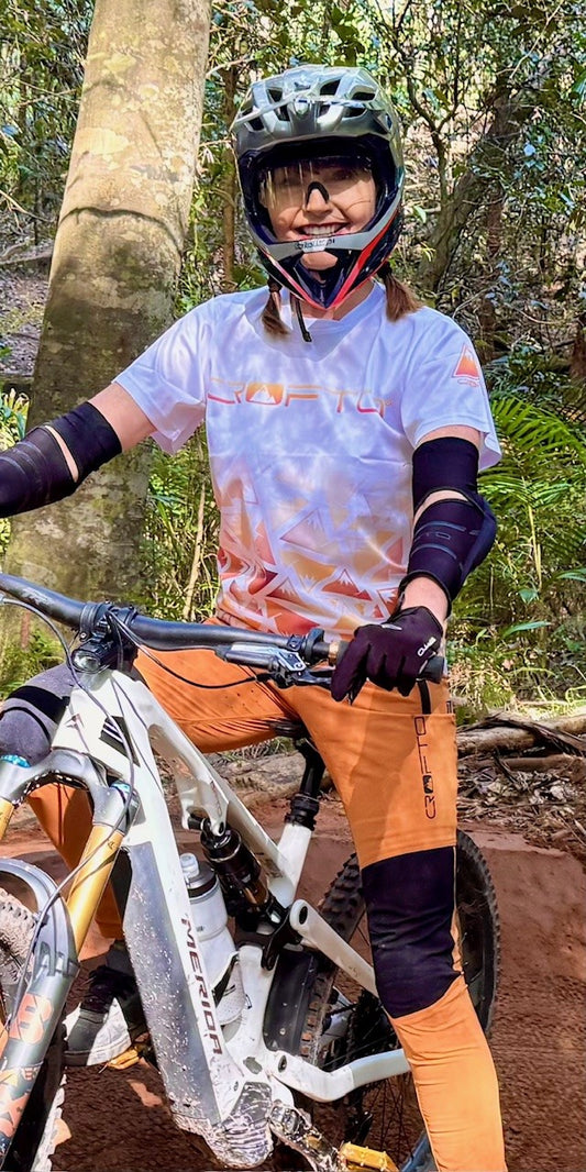 Woman on a mountain bike in a forest wearing a white and orange CROFTO MTB Jersey