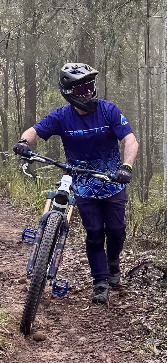 bike rider pushing mountain bike in forest wearing CROFTO jersey