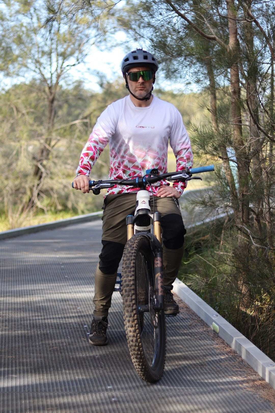 A man sitting on a mountain bike next to the forest wearing a CROFTO Mont Blanc Long Sleeve MTB jersey and dark green Amaroo pants
