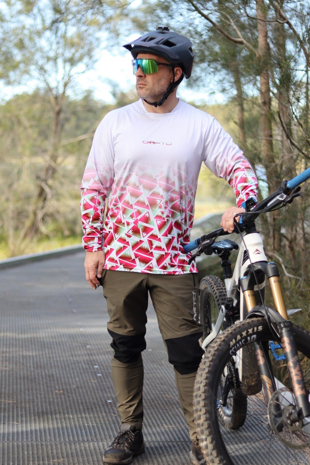 A man standing next to a mountain bike next to the forest wearing a CROFTO Mont Blanc Long Sleeve MTB jersey and dark green Amaroo pants