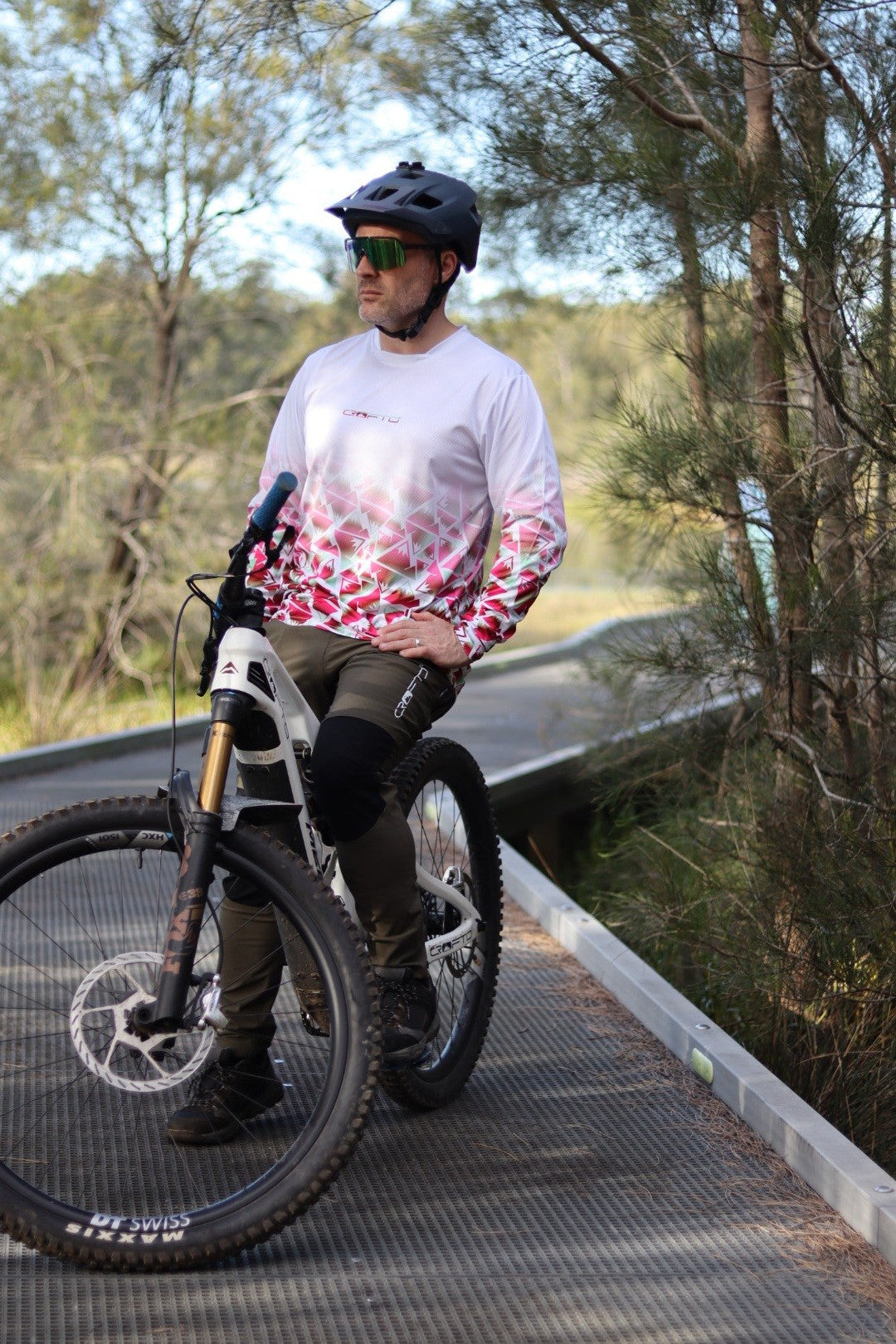 A man sitting on a mountain bike next to the forest wearing a CROFTO Mont Blanc Long Sleeve MTB jersey and dark green Amaroo pants