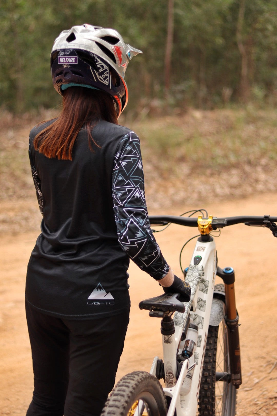 Person wearing a helmet and black cycling outfit with a mountain bike on a dirt path.