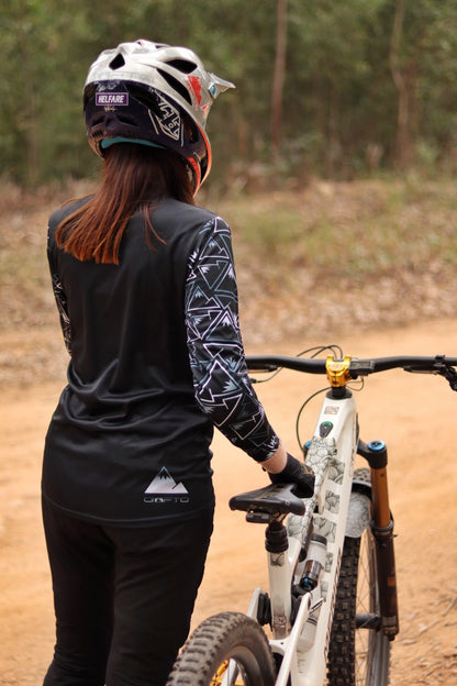 Person wearing a helmet and black cycling outfit with a mountain bike on a dirt path.
