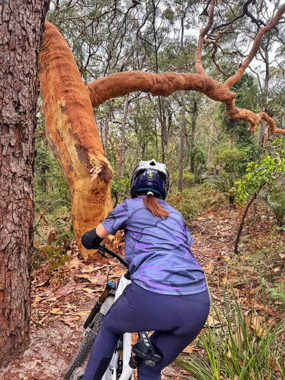 Person riding a bike through a forest with a large tree trunk in the foreground