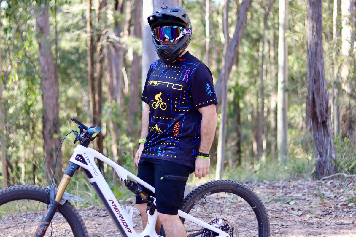 Mountain biker wearing the CROFTO Trail Maze jersey with blue and yellow gaming-inspired artwork during an outdoor trail riding session.