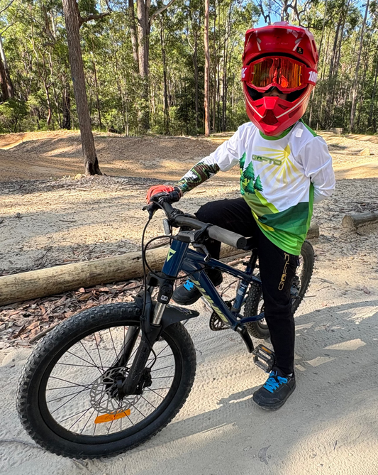 Young mountain biker wearing a red full-face helmet and CROFTO mountain bike jersey standing with a mountain bike on a forest trail in Australia.