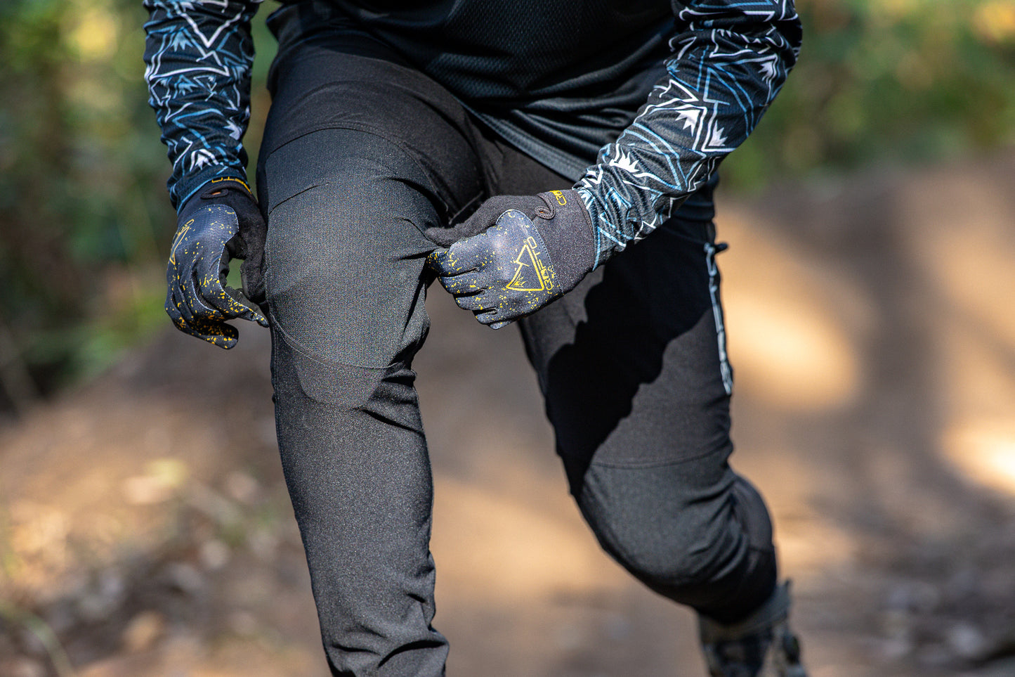 person in a forest wearing black crofto amaroo mtb pants pulling at the knee to check stretch. 