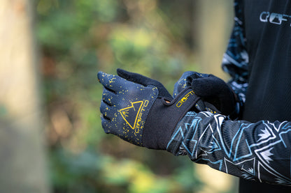 Close-up of a person wearing black and yellow CROFTO Apex Pro mountain biking gloves, with the brand logo and name clearly visible on the back of the glove.