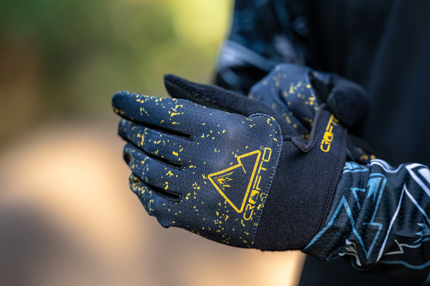 Close-up of a person wearing black and yellow CROFTO Apex Pro mountain biking gloves, with the brand logo and name clearly visible on the back of the glove.