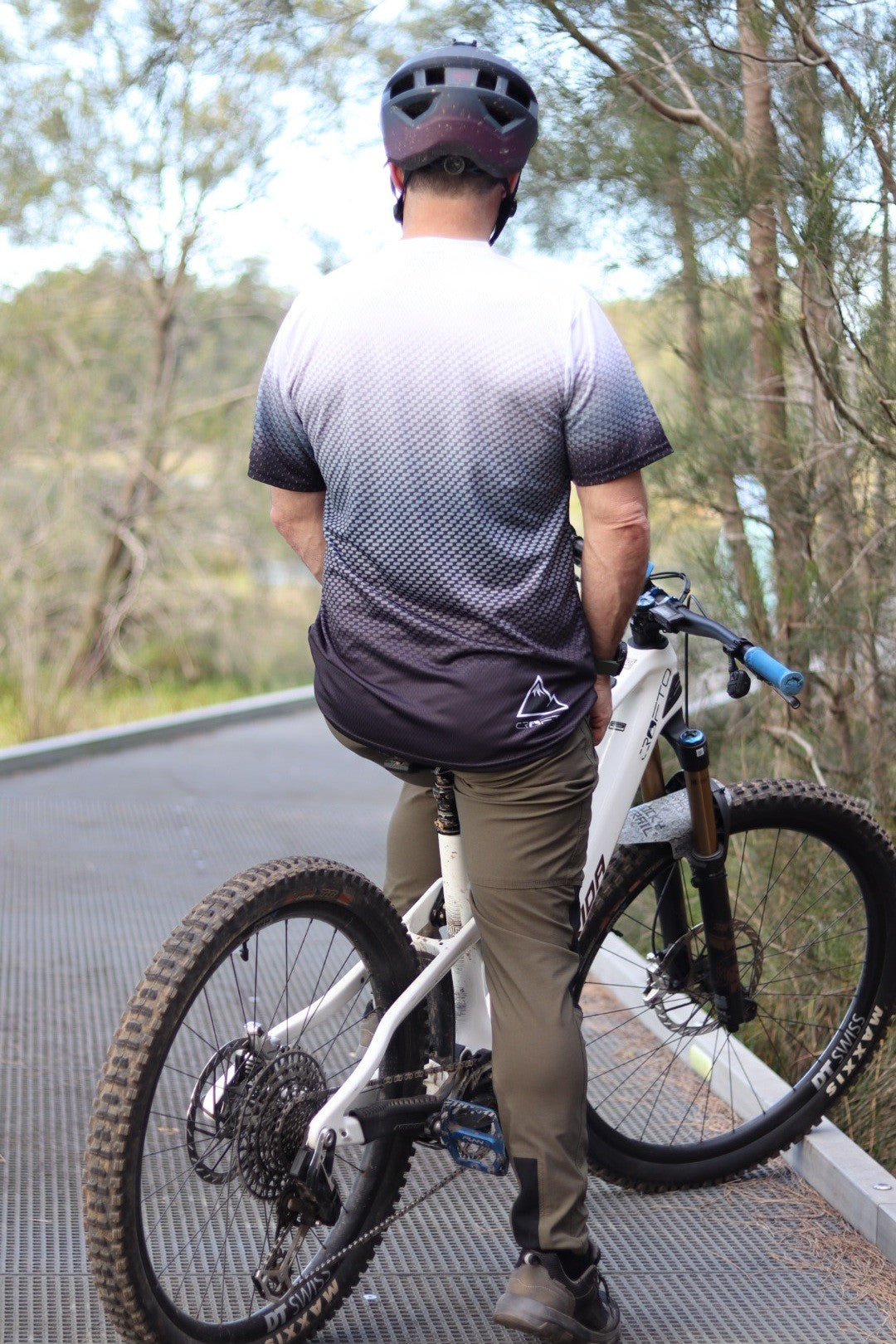 Back view of a man sitting on a mountain bike near the Australian forest wearing a navy helmet and CROFTO Carbon Classic mountain bike jersey and dark green Amaroo MTB pants