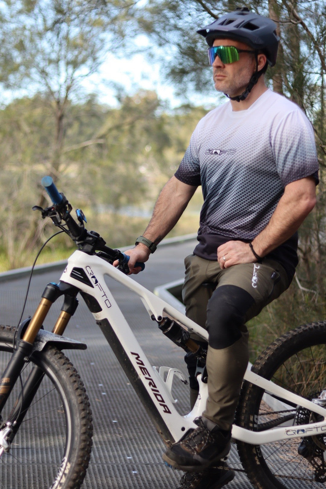 A man sitting on a mountain bike near the Australian forest wearing a navy helmet and CROFTO Carbon Classic mountain bike jersey and dark green Amaroo MTB pants