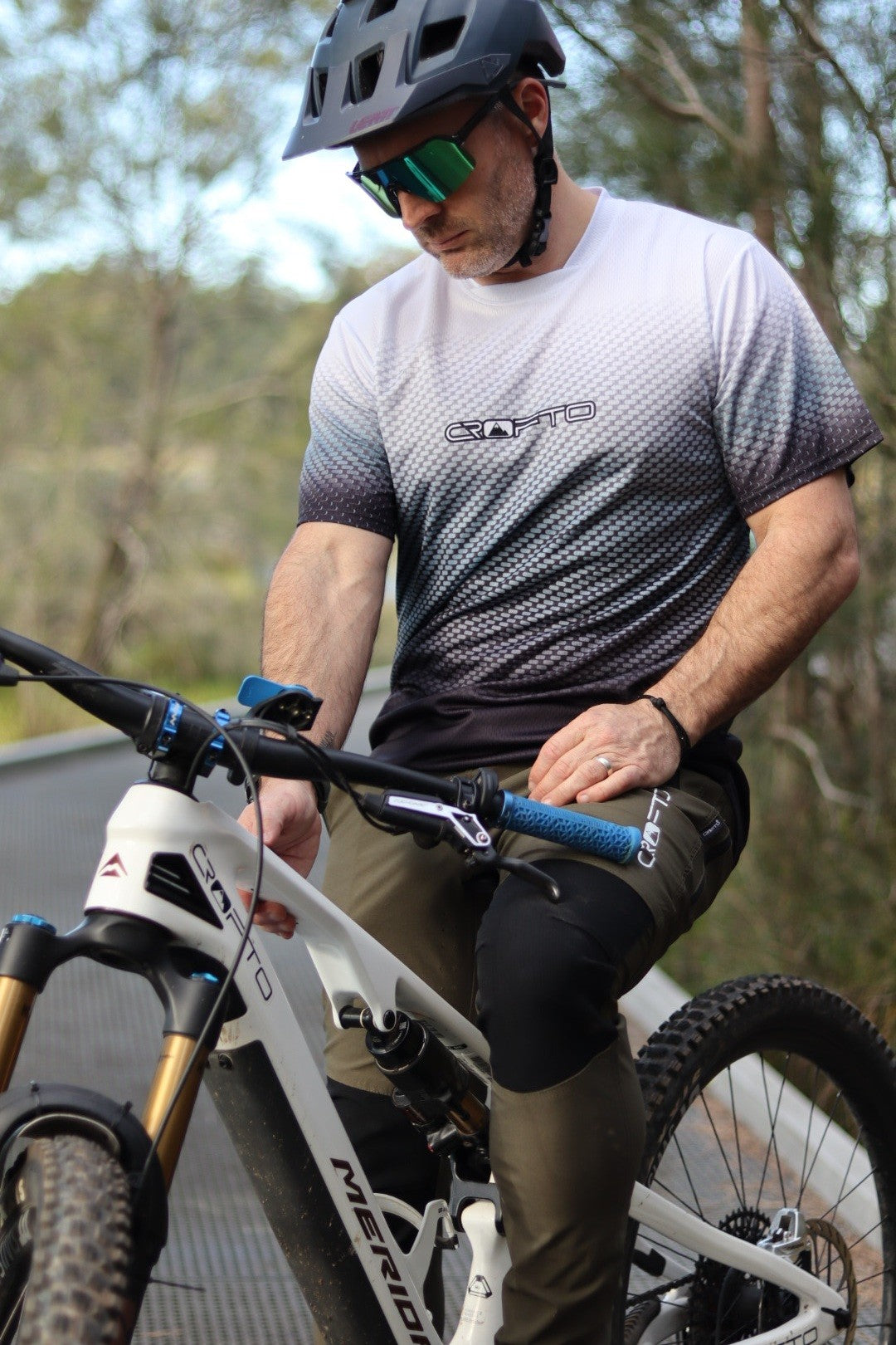 A man sitting on a mountain bike near the Australian forest wearing a navy helmet and CROFTO Carbon Classic mountain bike jersey and dark green Amaroo MTB pants