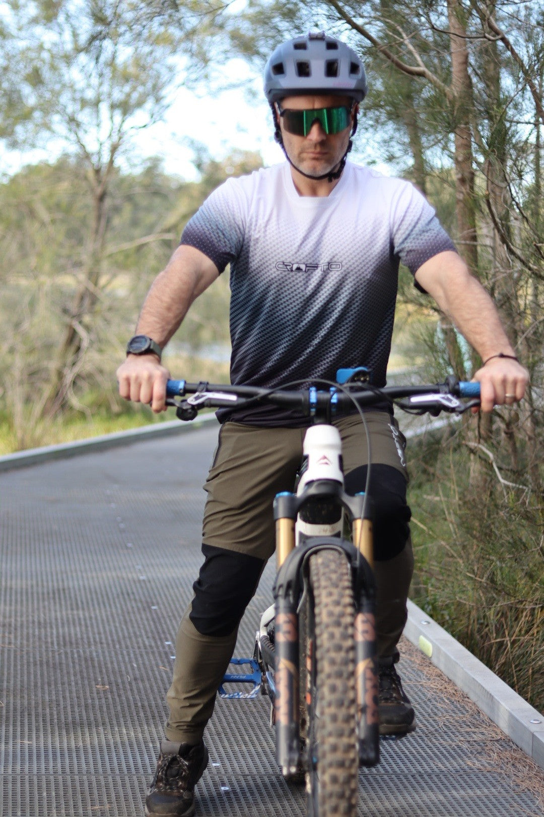 A man sitting on a mountain bike near the Australian forest wearing a navy helmet and CROFTO Carbon Classic mountain bike jersey and dark green Amaroo MTB pants