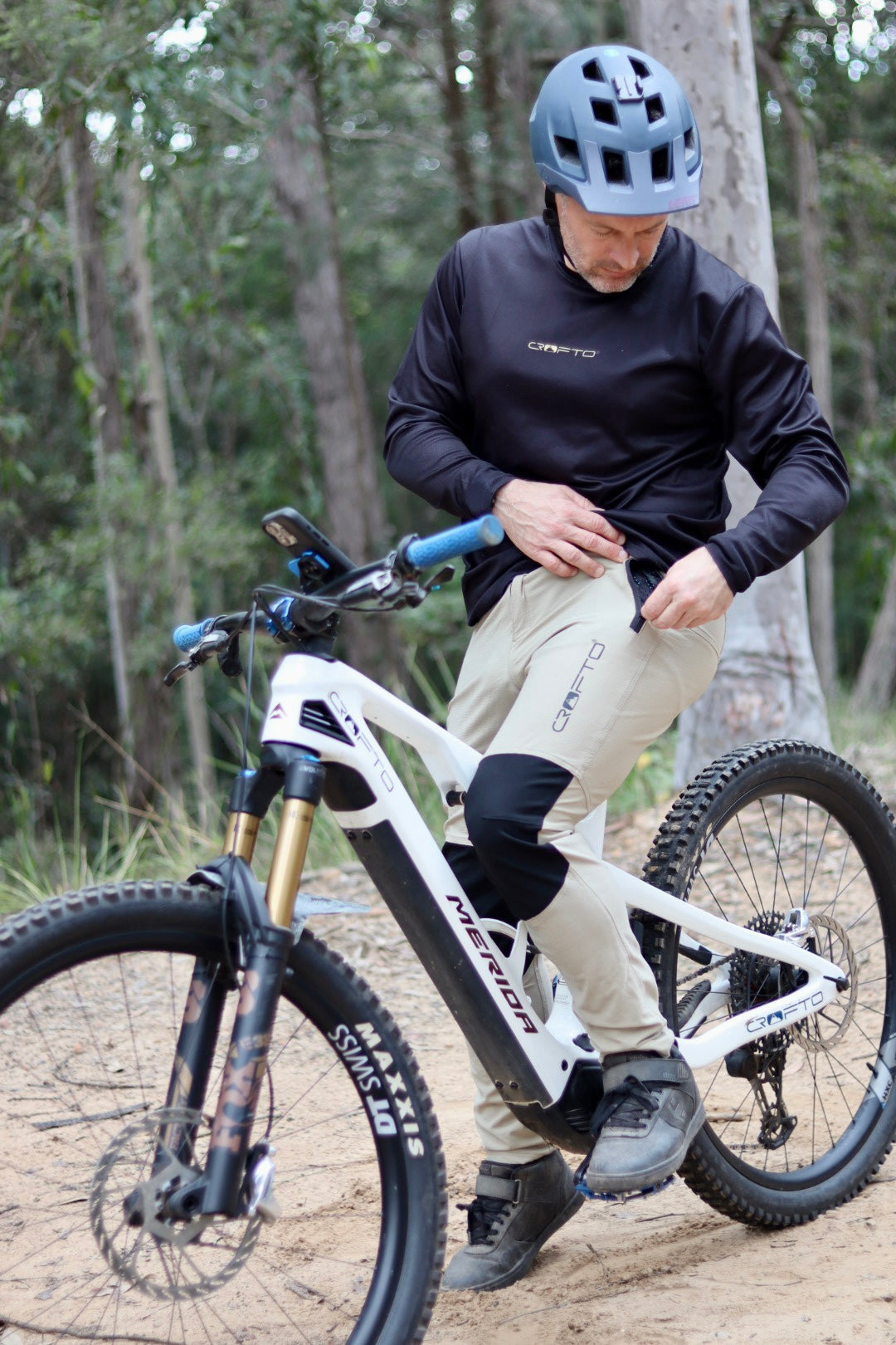Rider wearing CROFTO Amaroo MTB pants in sand colour sitting on a mountain bike on a dirt trail.