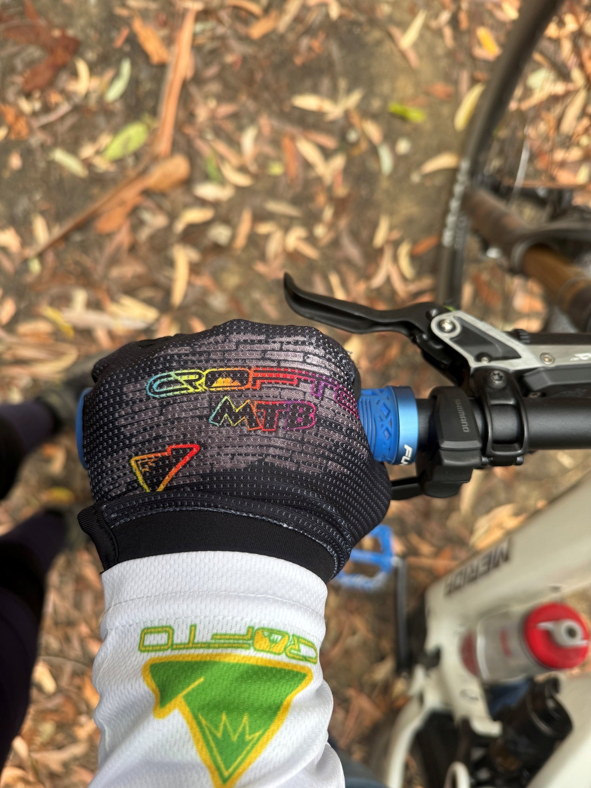 Close-up of a hand wearing crofto grafitti mtb gloves on a bike handlebar with a blurred natural background
