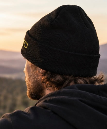Side profile of a male rider wearing a black CROFTO cuffed beanie overlooking a scenic mountain landscape.