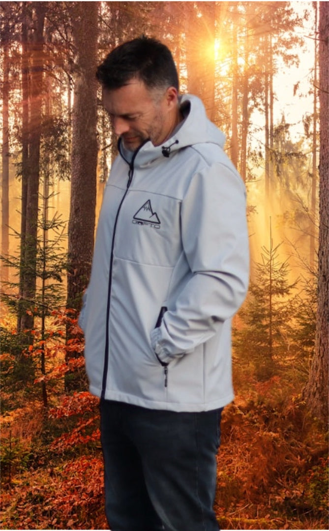Man wearing a light gray crofto soft shell jacket in a forest during sunrise.