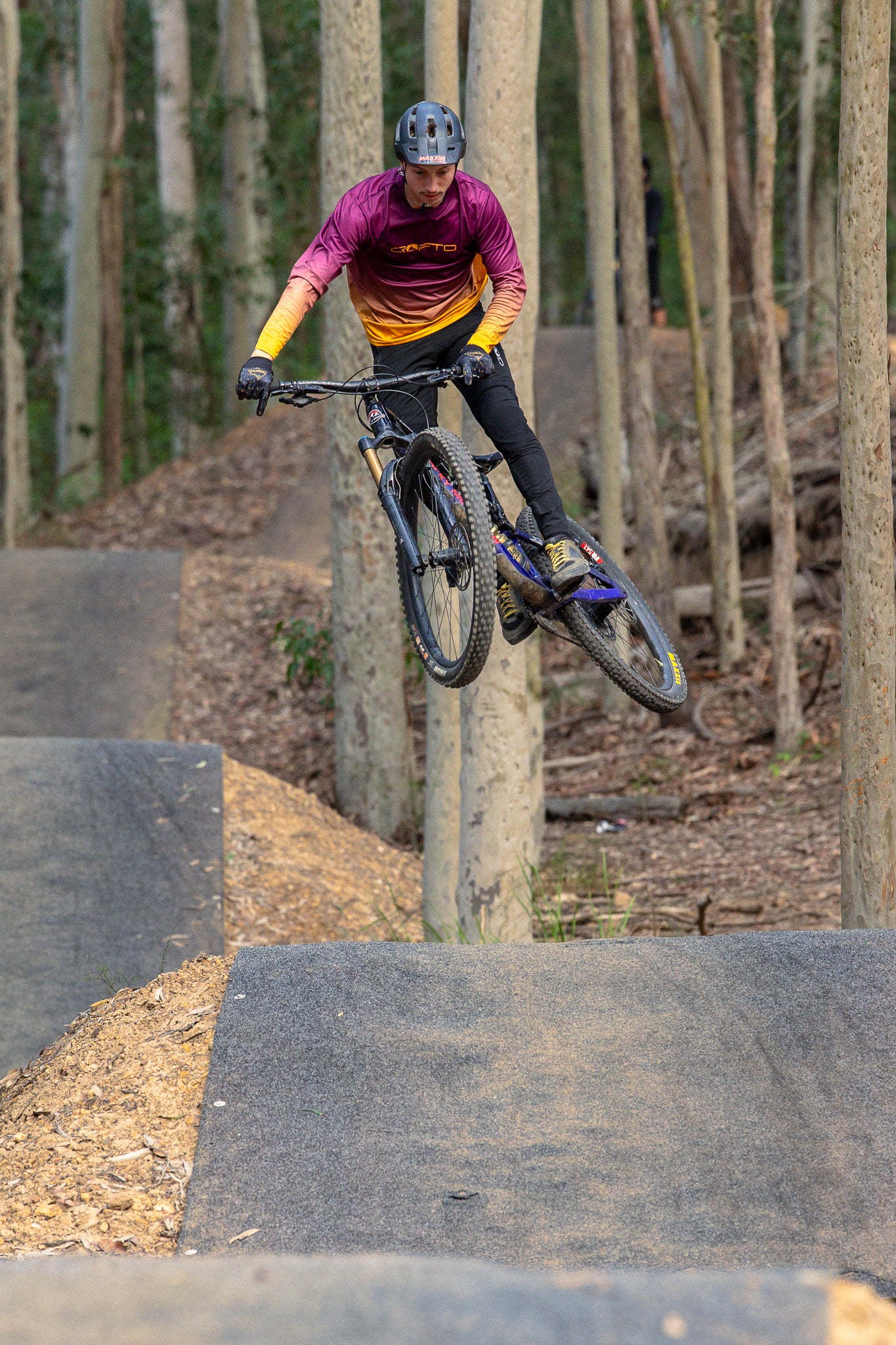 A mountain biker does a jump at ourimbah wearing crofto fade mtb jersey and amaroo pants